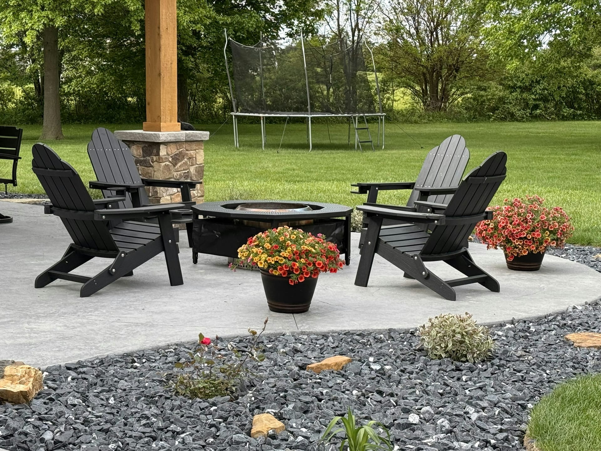 A stone patio and fire pit set on a wide, freshly mown lawn edged with mature trees