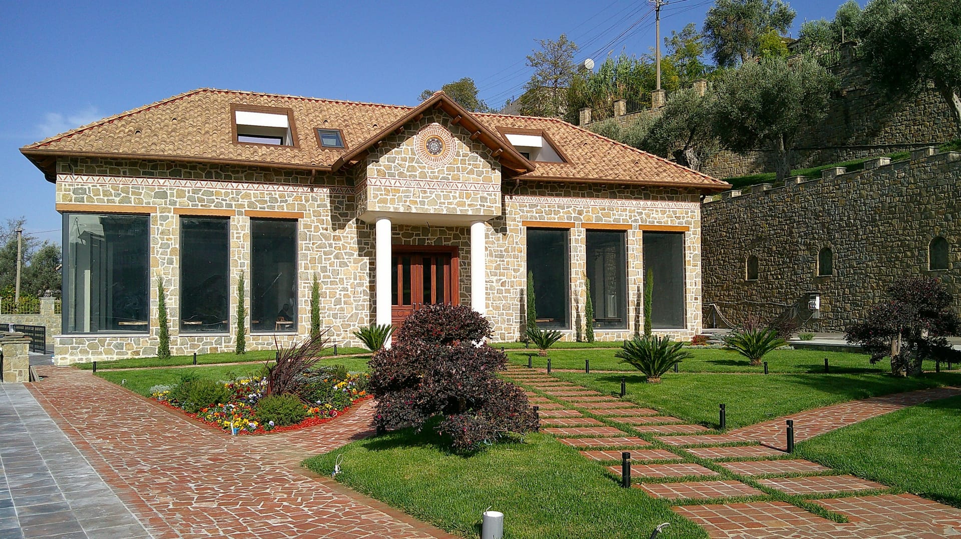 A stone house with paved walkways, clipped lawn and planted borders