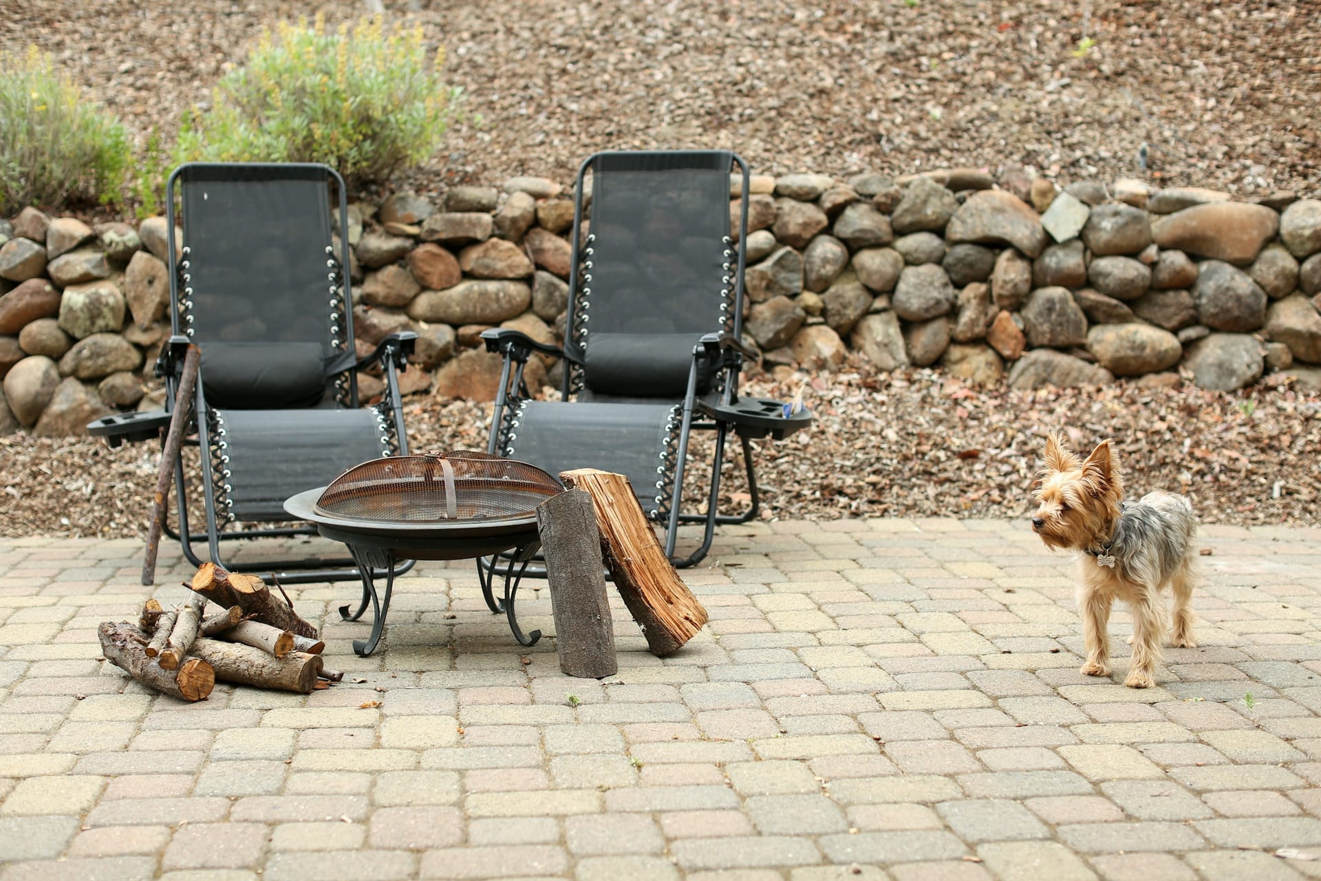A laid paver patio with seating and a fire bowl, backed by a fieldstone wall