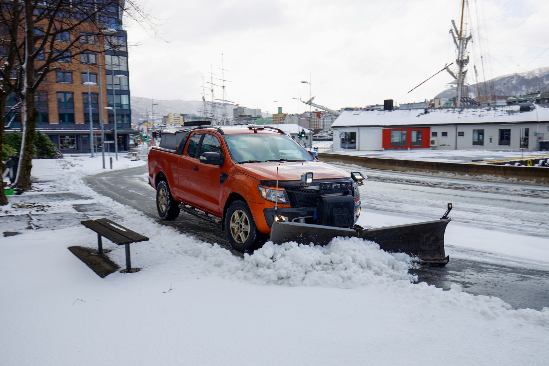 A pickup truck with a plow blade pushing snow clear of a road on a winter morning
